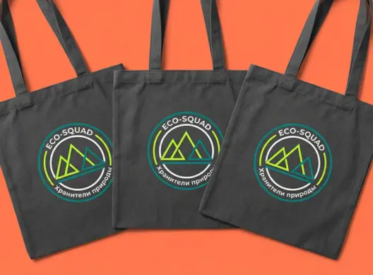Три тёмно-серые сумки-шопера ECO-SQUAD с логотипом в кислотно-зелёных цветах, расположены внахлёст под углом три четверти